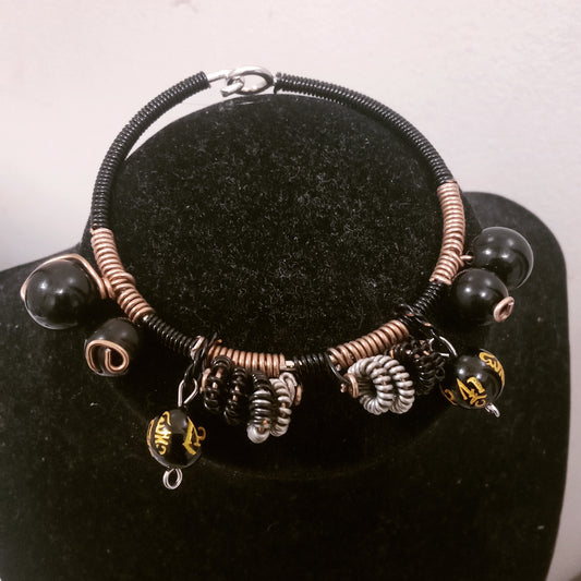 Wire wrapped beaded bracelet. Black round beads, black round beads with gold Chinese letters. Silver and black wire wrapped spiral charms. Hook and eye closure