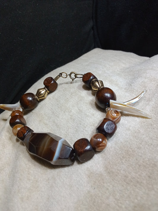 Dark toned glass bead center piece, with wood beads, silver plated gold colored space beads and natural shell beads in the shape of claws. Modified lobster claw clasp. 9 inches on length.